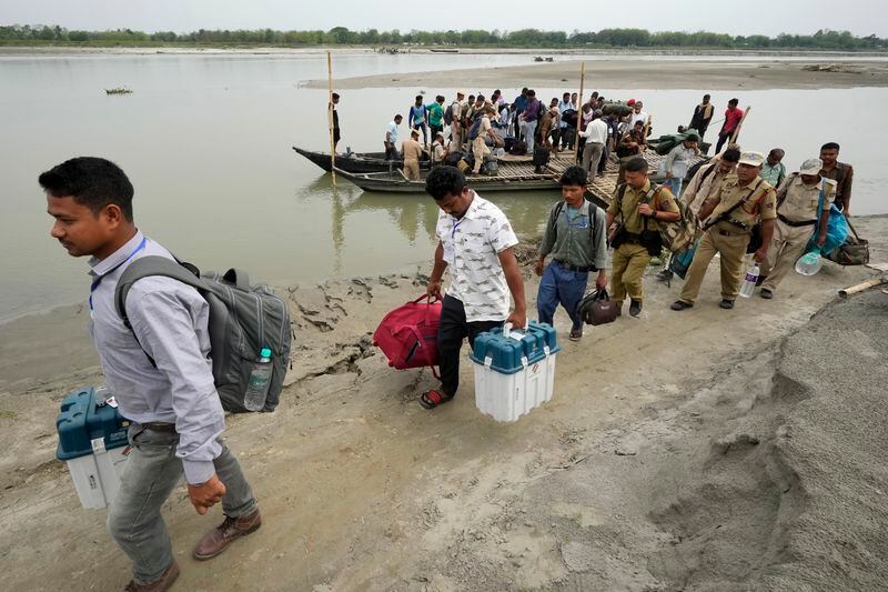 Polling officials and security personnels carry Electronic Voting Machines (EVMs) and other election material off a boat after crossing the Brahmaputra river on the eve of the national election at Baghmora Chapori (small island) of Majuli, about 350km (218 miles) east of the state capital Guwahati, India, Thursday, April 18, 2024. (AP Photo/Anupam Nath)