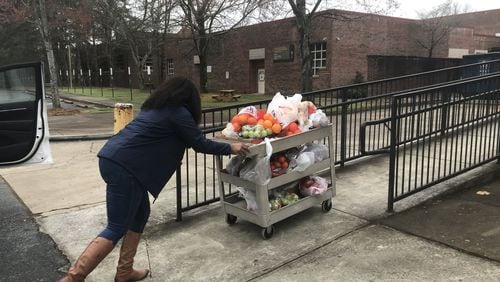 Jasmine Crowe, founder of Goodr, pushes a cart full of fruit into Phoenix Academy, the former Crim High School, on Monday to prepare for the first day of food distribution at Atlanta Public Schools. Goodr partnered with APS to set up sites for students to get food while school buildings are closed. VANESSA McCRAY/AJC