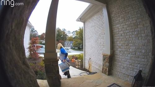 The video shows a woman park her car in the driveway, walk up to the steps of the home and steal the packages hidden behind a post.