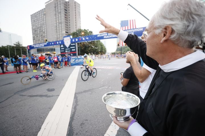 Rev. Samuel Candler of the The Cathedral of St. Philip blesses runners with holy water at the 53rd running of the Atlanta Journal-Constitution Peachtree Road Race in Atlanta on Sunday, July 3, 2022. (Miguel Martinez / Miguel.Martinezjimenez@ajc.com)