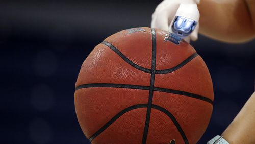 An worker waves an ultra violet lamp over the ball to kill germs during an NCAA basketball game. (Butch Dill/AP)