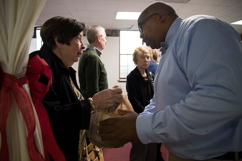 Lillian Rice, of First Baptist Church of Christ on High Place, hands the food she brought to Jimmie Smith, a deacon at First Baptist Church on New Street, at First Baptist Church's Thanksgiving Potluck on Sunday, Nov. 19. (Jenna Eason / for the AJC)
