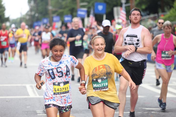 Runners hold hands as they finish the 54th running of the Atlanta Journal-Constitution Peachtree Road Race in Atlanta on Tuesday, July 4, 2023.   (Jason Getz / Jason.Getz@ajc.com)