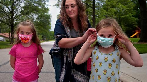 Jenny Berla helps her twins Isla, left, and Elodie with their masks as they approach their sister's school to pick her up after class on Wednesday, May 19, 2021. Berla, who is planning to send the girls to kindergarten this fall, is concerned that dropping mask mandates before young children are eligible for vaccinations leave them open to risk. (Robert Cohen/St. Louis Post-Dispatch/TNS)