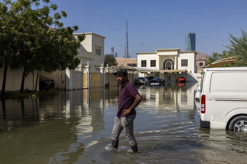 A man walks through standing floodwater caused by heavy rain with the Burj Khalifa, the world's tallest building, seen in Dubai, United Arab Emirates, Thursday, April 18, 2024. The United Arab Emirates attempted to dry out Thursday from the heaviest rain the desert nation has ever recorded, a deluge that flooded out Dubai International Airport and disrupted flights through the world's busiest airfield for international travel. (AP Photo/Christopher Pike)