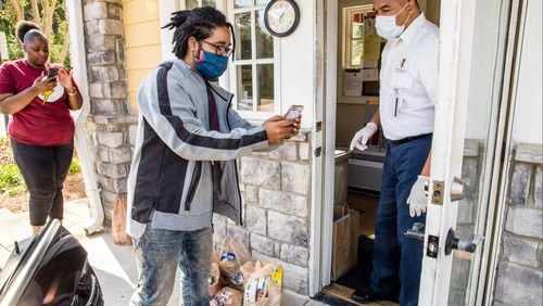 Instacart gig worker Kyle Ford, center, delivers groceries to Larry Jones, right, Park Spring retirement community’s security officer, and shares the customer address Tuesday, April 28, 2020 in the Stone Mountain area. (Jenni Girtman for Atlanta Journal-Constitution)