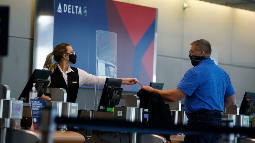 FILE - In this July 22, 2020 photo, a ticketing agent for Delta Airlines hands a boarding pass to a passenger as he checks in for a flight in the main terminal of Denver International Airport in Denver. .Air travel has collapsed because of the virus pandemic, and airlines are trying to convince passengers and their own employees about safety. All airlines require passengers to wear masks during flights, and most extend the rule to airports too. But some people have complained about violators refusing to keep their mask on .(AP Photo/David Zalubowski)