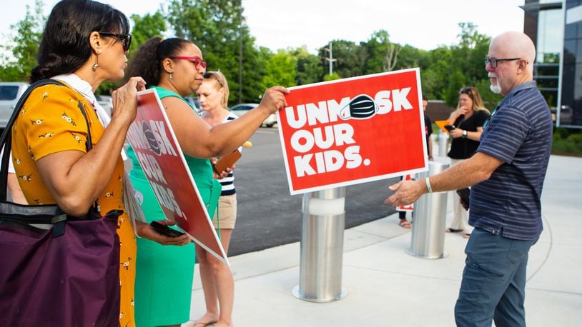 Billy Cahill (far right) hands a woman his "unmask our kids" sign to pose for a photo outside of the Cobb County School District office on Thursday, May 20, 2021, in Marietta, Georgia . Many community members waited in line to speak at the school board meeting to voice their support for unmasking.  CHRISTINA MATACOTTA FOR THE ATLANTA JOURNAL-CONSTITUTION