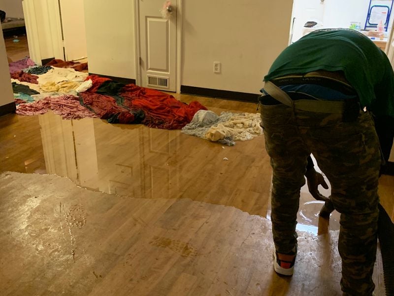 A neighbor helps mop up Miracle Fletcher's apartment at Trestletree Village in Atlanta after it was flooded by sewage in 2019. (Contributed)