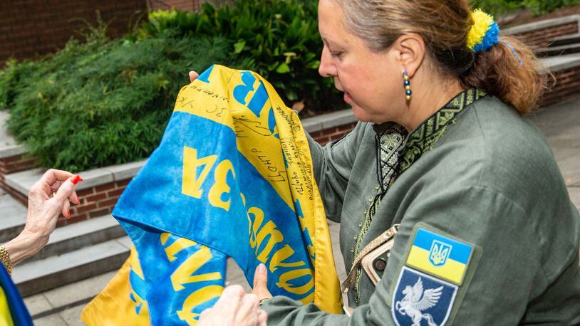 Ukrainian Chaplin Olga Westfall brings a flag signed by soldiers to One Day for Ukraine morning blessings at All Saints’ Episcopal Church on Wednesday, Aug 24, 2022, Ukraine’s Independence Day.  Other Ukrainian refugees, activists and humanitarians gather to show continued support for Ukraine and share stories that bombing began again overnight.  HelpingUkraine.us continues to provide medical equipment, housing, clothing and support to people fighting and living in the war-torn country.  (Jenni Girtman / ABO Associates / HelpingUkraine.Us)