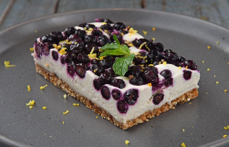 Start a new summer tradition with Blueberry Lemon Cheesecake, shown here with lemon zest and mint leaf garnish. (Styling by Claudine Molson-Sellers / Chris Hunt for the AJC)