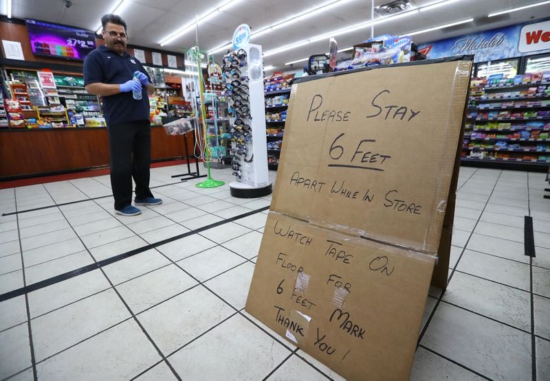 Ejaz Tarar stands next to his makeshift sign keeping customers 6 feet apart while cleaning the inside of the Food Mart in Newton County on Thursday, March 26, 2020, in Newborn, Georgia. The store put down tape to mark 6-foot barriers for customers. (Curtis Compton / ccompton@ajc.com)