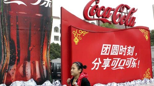 Coca-Cola Company’s chief executive said some Coke manufacturing plants in China were shuttered in the wake of the latest coronavirus, but the company is contemplating some re-openings to safely meet the population’s needs. In this 2010 photo, a woman walks past a Coke advertisement in central China’s Hubei Province. China is a major market for the Atlanta-based company.