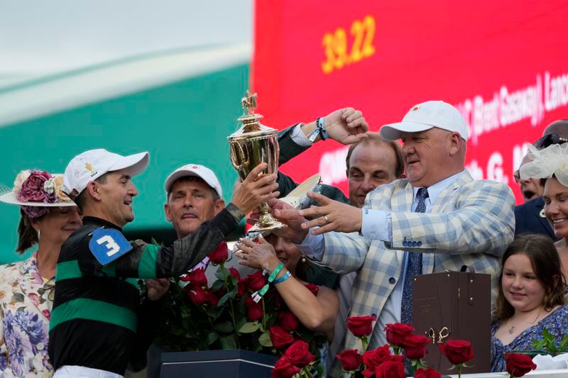 Trainer Kenneth McPeek, right, hand off the trophy to jockey Brian Hernandez Jr. as Hernandez celebrates in the winner's circle after riding Mystik Dan to win the 150th running of the Kentucky Derby horse race at Churchill Downs Saturday, May 4, 2024, in Louisville, Ky. (AP Photo/Jeff Roberson)