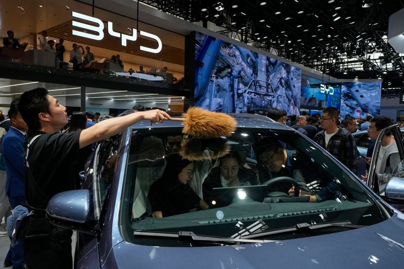 A worker wipes as visitors sit on a BYD Song Pro DM-i car model during the Auto China 2024 in Beijing, Sunday, April 28, 2024. Global automakers and EV startups unveiled new models and concept cars at China's largest auto show, with a focus on the nation's transformation into a major market and production base for digitally connected, new-energy vehicles. (AP Photo/Andy Wong)