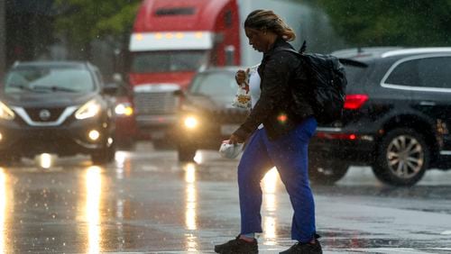 A woman walks in the rain as she crosses Peachtree road near Phipps Plaza in Buckhead, Thursday, May 9, 2024, in Atlanta. (Jason Getz / AJC)
