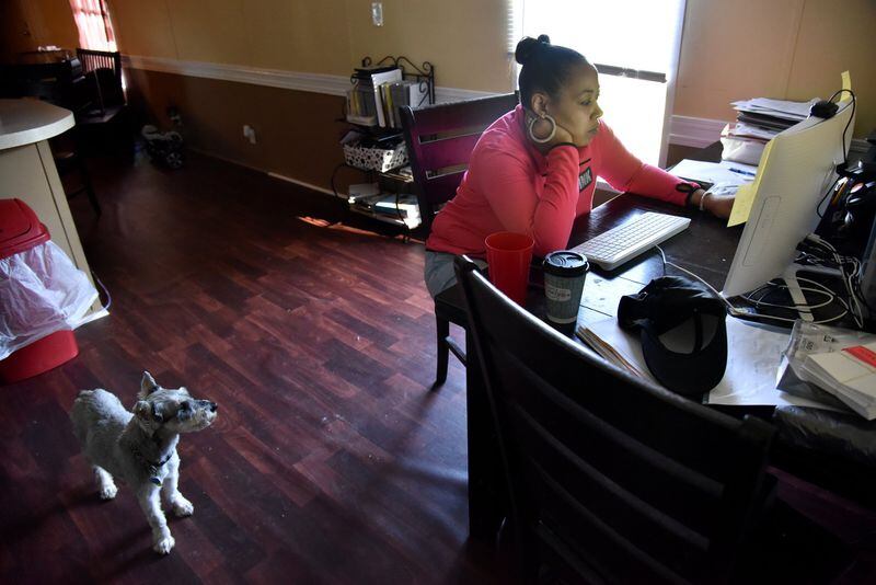 Priscilla Vetaw applies online for a job at a nearby Walmart store as her dog Karmello looks on. She kept the lights off in her living room to save on electricity. HYOSUB SHIN / HSHIN@AJC.COM
