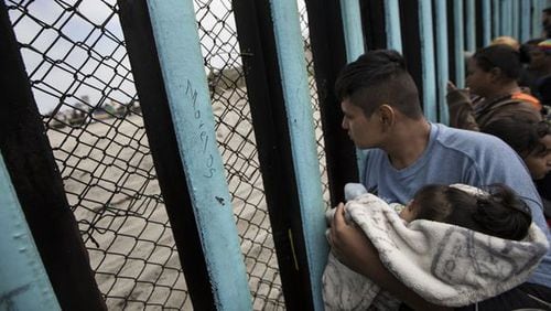 A member of the Central American migrant caravan, holding a child, looks through the border wall toward a group of people gathered on the U.S. side in April. (Photo: Hans-Maximo Musielik, AP)