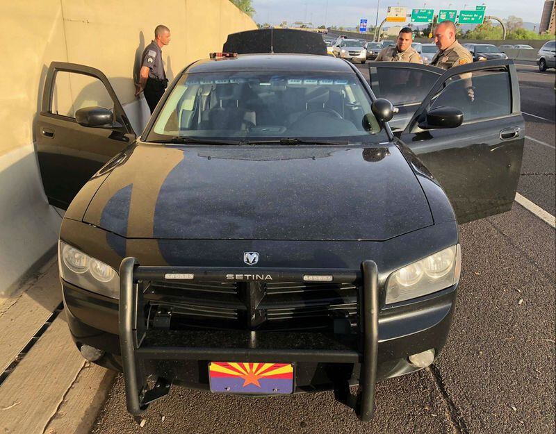 Arizona state troopers inspect the personal vehicle of Matthew Allen Disbro, seen behind the car at left, after Disbro allegedly tried to use his Dodge Charger to pull the troopers over as they patrolled a highway in an unmarked Ford Mustang Wednesday, July 11, 2018. The Charger was equipped with police lights, a siren and a police scanner. Disbro, who was charged with impersonating an officer, works as a uniformed, armed security guard, according to investigators.