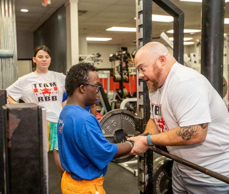 Dave Githutu, a Milton High School weight-lifter who regularly competes in the special olympics, trains at Roswell Barbell with his coach Josh Porter on Tuesday, Aug 23, 2022 and team members.  The athlete is competing in England in September at an able-bodied competition before a scheduled heart surgery scheduled for Spring.  (Jenni Girtman for The Atlanta Journal-Constitution)