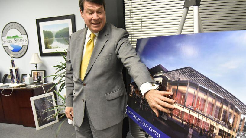 Rusty Paul, mayor of Sandy Springs, shows off concept photographs of new Sandy Springs City Center at his office. For years, the city of Sandy Springs was held up as a model for how to keep government efficient by outsourcing almost all services to private companies. Now, the young city of Stonecrest is looking to copy Sandy Springs, while South Fulton is launching with a more traditional government. HYOSUB SHIN / HSHIN@AJC.COM