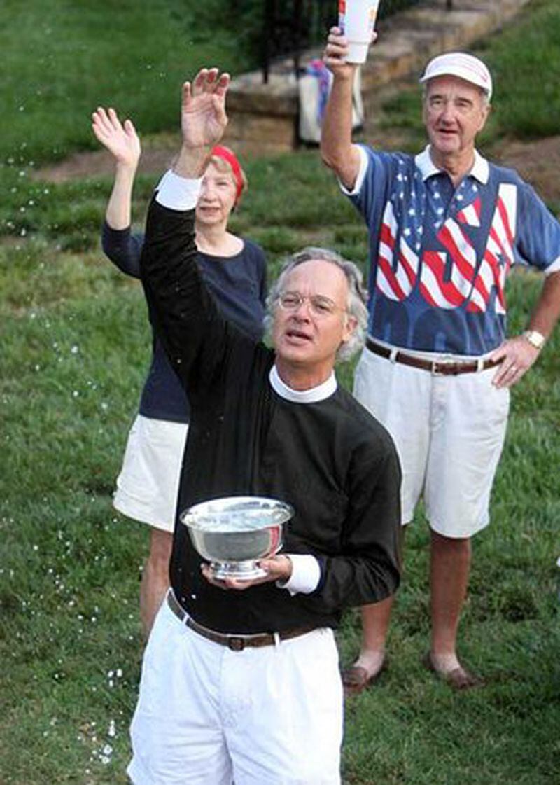 Dean Sam Candler, of The Cathedral of St. Philip, tosses holy water in the air as elite runners go by in front of the cathedral on Peachtree Road.