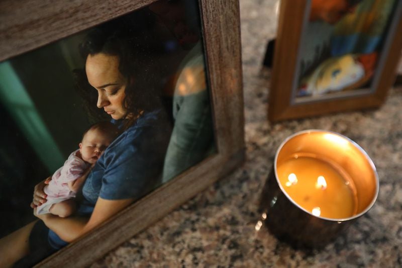 A candle burns next to a family portrait of Kaitlin Hunt and her infant, Riley, who were struck in September 2017 in downtown Woodstock. They and family friend Kathy Deming died of their injuries. Curtis Compton/ccompton@ajc.com