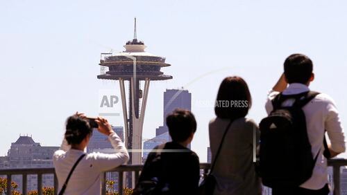 Tourists look across at the Space Needle, where a floor of scaffolding remains below the upper portion, in Seattle on Tuesday, May 22, 2018. The family-owned landmark is set to unveil the biggest renovation in its 56-year history next month, a $100 million investment in a single year of construction that transformed the structure's top viewing level some 500-feet above ground. (AP Photo/Elaine Thompson)