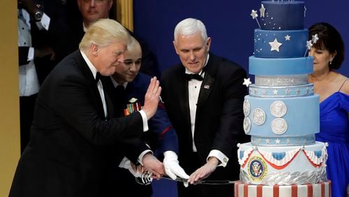 President Donald J. Trump, left, and Vice President Mike Pence, right, are helped by Coast Guard Petty Officer 2nd Class Matthew Babot, center, as they cut a cake at The Salute To Our Armed Services Inaugural Ball Friday, Jan. 20, 2017, in Washington. (AP Photo/David J. Phillip)
