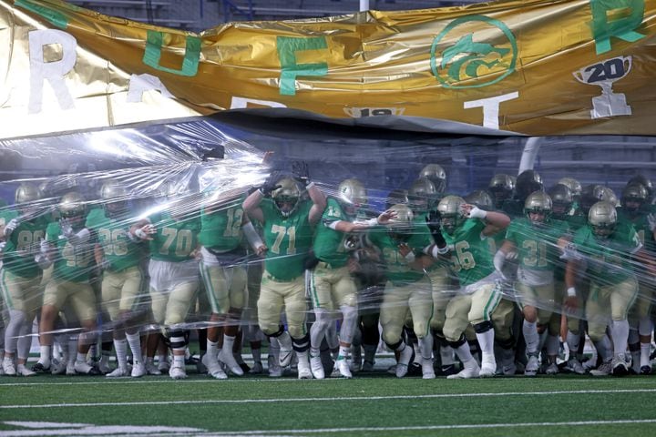 Buford players burst through the banner before their game against Langston Hughes in the Class 6A state title football game at Georgia State Center Parc Stadium Friday, December 10, 2021, Atlanta. JASON GETZ FOR THE ATLANTA JOURNAL-CONSTITUTION