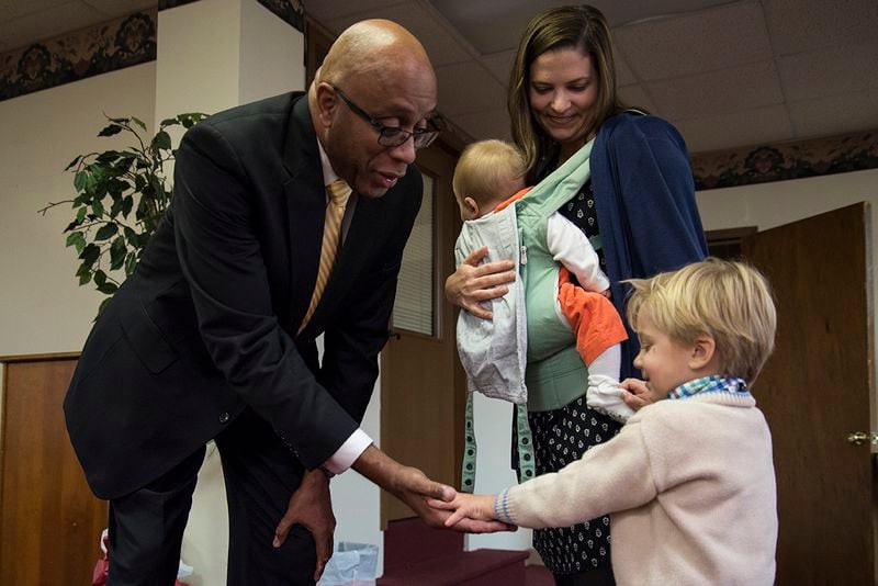 Pastor James Goolsby of First Baptist Church on New Street gives Billy a high five while his mother, Audrey Dickison, watches with her youngest son, Mac, in her arms on Sunday, Nov. 19 at First Baptist Church's Thanksgiving Potluck. Dickison is the wife of Scott Dickison, the reverend at First Baptist Church of Christ on High Place. (Jenna Eason / for the AJC)