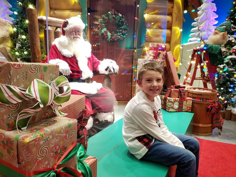 Visits to Santa at metro Atlanta malls and stores during the pandemic are often still happening, but with a slate of new precautions in place. Among the additions: masks, temperature checks and physical barriers. On a recent visit, a clear plastic wall separated seven-year-old Brayden Long from Santa, wearing a face shield, at the Bass Pro Shops store in Duluth. MATT KEMPNER / AJC