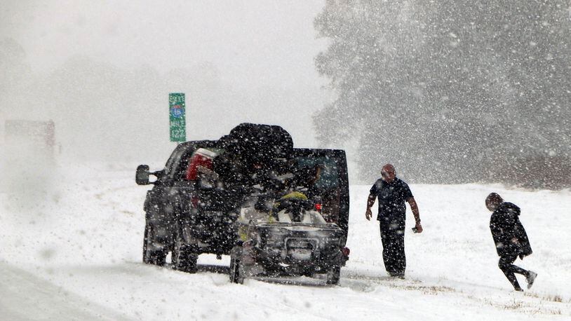 People attend to their vehicle on Interstate 16, near Savannah, Ga., on Wednesday, Jan. 3, 2018. A brutal winter storm dumped snow in Tallahassee, Fla., on Wednesday for the first time in nearly three decades before slogging up the Atlantic Coast and smacking Southern cities such as Savannah and Charleston, S.C., with a rare blast of snow and ice.