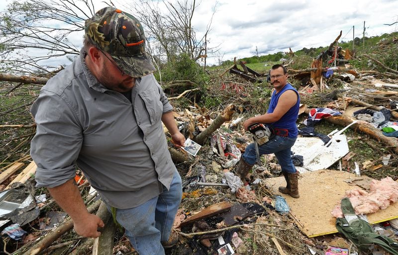 April 13, 2020 Chatsworth: Justin Tallent (left) salvages photographs from the remains of his cousinâs trailer in the Deer Park trailer park while James Bailey mans a chain saw after a deadly tornado killed at least 7 in Murray County on Monday, April 12, 2020, in Chatsworth.   Curtis Compton ccompton@ajc.com