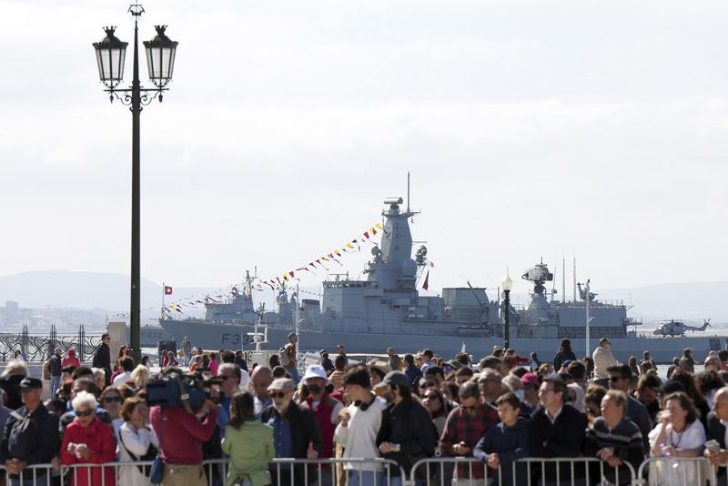Portuguese Navy frigates Dom Francisco de Almeida and Corte-Real, left, are anchored in the Tagus river by Lisbon's Comercio square, Thursday, April 25, 2024, while people watch celebrations of the fiftieth anniversary of the Carnations Revolution. The April 25, 1974 revolution carried out by the army restored democracy in Portugal after 48 years of a fascist dictatorship. (AP Photo/Ana Brigida)