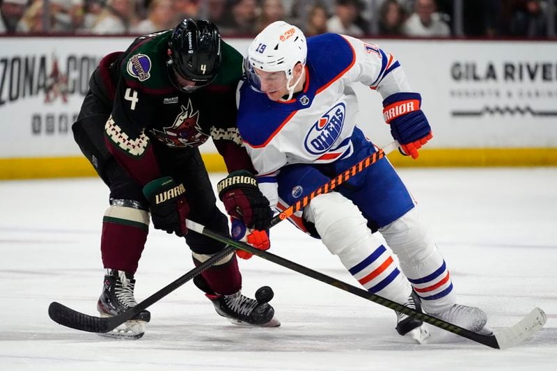 Edmonton Oilers center Adam Henrique (19) and Arizona Coyotes defenseman Juuso Valimaki (4) vie for the puck during the second period of an NHL hockey game Wednesday, April 17, 2024, in Tempe, Ariz. (AP Photo/Ross D. Franklin)
