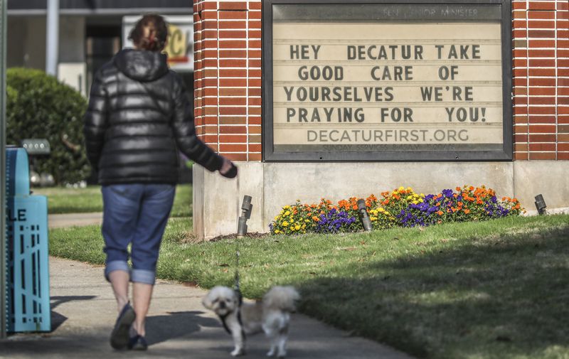 In this late March file photo, Marcia Soldat walks her dog, Duke, past a sign offering prayer support to the community posted in front of Decatur First United Methodist Church, 300 East Ponce de Leon Ave. JOHN SPINK/JSPINK@AJC.COM