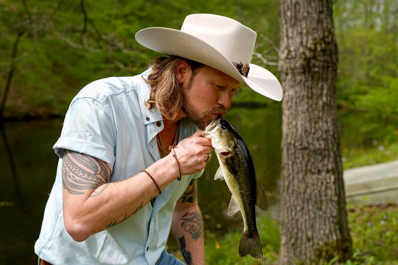 Brian Kelley kisses a fish he caught from a pond outside his cabin Wednesday April 17, 2024, in Nashville, Tenn. (AP Photo/George Walker IV)