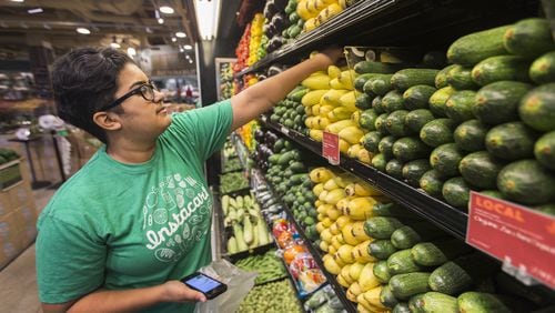 Instacart employee checks phone for list of customer orders while picking out items at a Whole Foods. (AJC file photo)