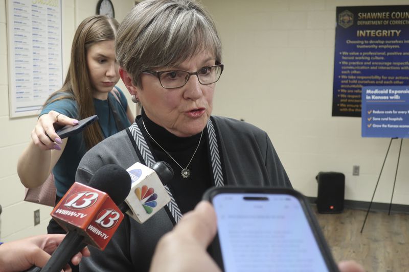 Kansas Gov. Laura Kelly answers questions from reporters following an event at the Shawnee County, Kan., jail, Tuesday, April 16, 2024, in Topeka, Kan., as her communications coordinator, Grace Hoge, watches behind her. Kelly has not made a decision on whether she'll sign or veto a bill that restricts diversity, equity and inclusion initiatives on state university campuses. (AP Photo/John Hanna)