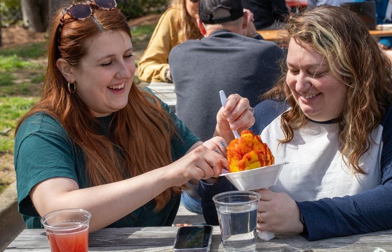 Angela Freeman (left) and Ivey Lail of Sandy Springs share a sweet and salty mango at Bien Vegano Atlanta, a monthly market featuring artists, food and producers of vegan items. Jenni Girtman for The Atlanta Journal-Constitution
