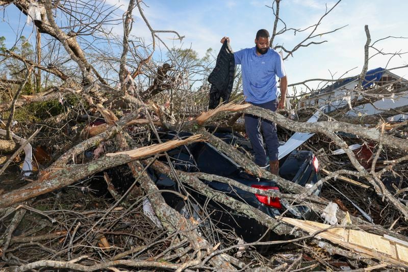Standing on his daughter’s car, David Rhodes, of LaGrange, pulls a jacket the automobile that was destroyed by falling trees at ground zero of the tornado damage, Monday, March 27, 2023, in West Point, Ga.. Rhodes’ daughter Mac Rhodes was at a nearby beauty salon Sunday morning when the tornado came through and destroyed the salon and her car. She along with the two other people were not seriously injured. Jason Getz / Jason.Getz@ajc.com)

