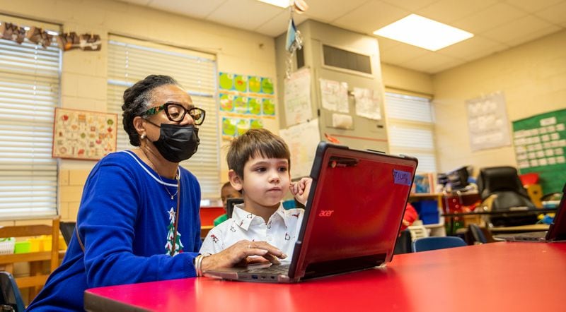 Sarah Finch, an ESOL teacher, helps Yurii Slasnyi in his kindergarten classroom at Briar Vista Elementary School on Thursday, Dec 15, 2022.  Yurii and his mother are working to secure healthcare, housing and other basics.  (Jenni Girtman for The Atlanta Journal-Constitution)