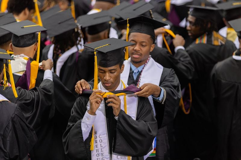 Graduates help each other don hoods at the commencement ceremony at Morehouse in Atlanta on Sunday, May 19, 2024. (Arvin Temkar / AJC)