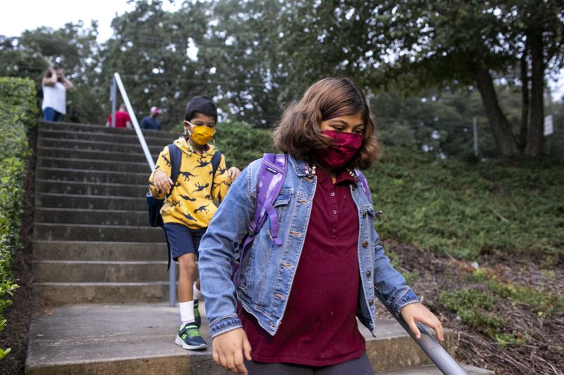 In this file photo, Dahlia and Omar Varghese walk to Burgess Elementary School in East Atlanta. Dahlia caught COVID-19 during the first week of school about a month ago. (Rebecca Wright for The Atlanta Journal-Constitution)