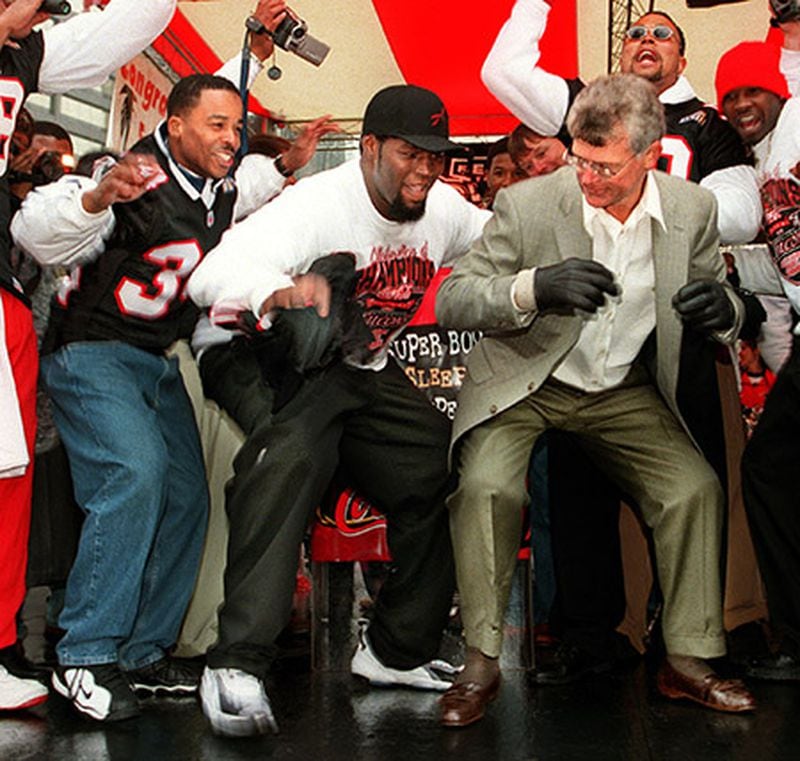 Players Ray Buchanan (left) and Bob Whitfield (center) dance the "dirty bird" with coach Dan Reeves in Woodruff Park at the finale of a city wide parade for the Super Bowl Falcons. (AJC)