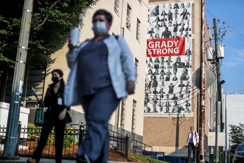 Medical workers arrive Tuesday, Aug. 10, at Grady Memorial Hospital against a large banner draped across the facade of a parking deck. COVID-19 cases are filling Georgia hospitals once again, igniting concerns of even more devastating outbreaks to come. (John Spink / John.Spink@ajc.com)

