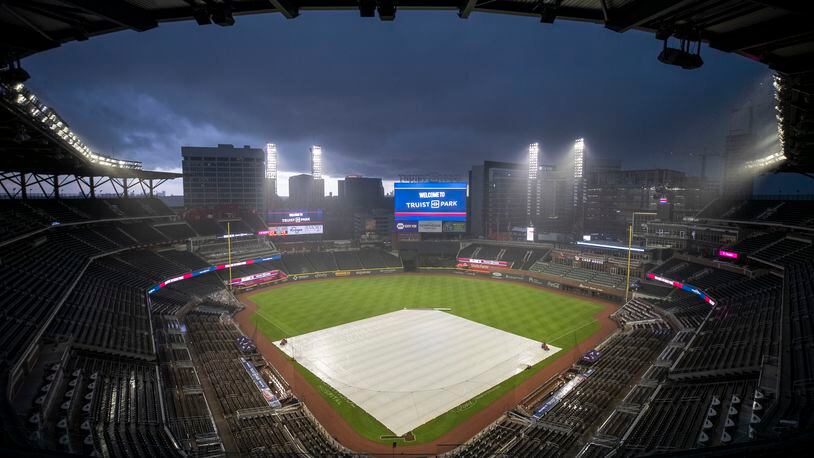 A tarp covers the field as a thunderstorm produces heavy rain in a spectator-free stadium. (ALYSSA POINTER / ALYSSA.POINTER@AJC.COM)