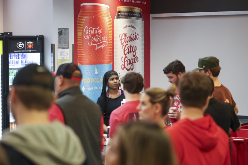 A poster for Creature Comfort Brewing Company is shown on the wall of a concession as employees sell beer to Georgia fans before Georgia’s men’s basketball game against Alabama at Stegemen Coliseum, Wednesday, January 31, 2024, in Athens, Ga. (Jason Getz / jason.getz@ajc.com)