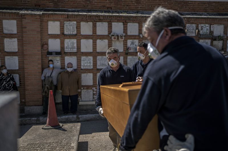 The daughter and husband, center left, no names available, of an elderly victim of the COVID-19 coronavirus stand as undertakers place the coffin in the grave at the Almudena cemetery in Madrid.